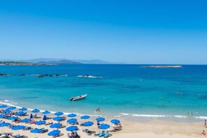 A beach with clear blue waters, a boat, and numerous blue umbrellas. - Pilot Lux Apartment (Chania)