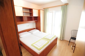 Una cama doble con cabecera de madera y estanterías empotradas, una pequeña silla y una ventana con cortinas.
