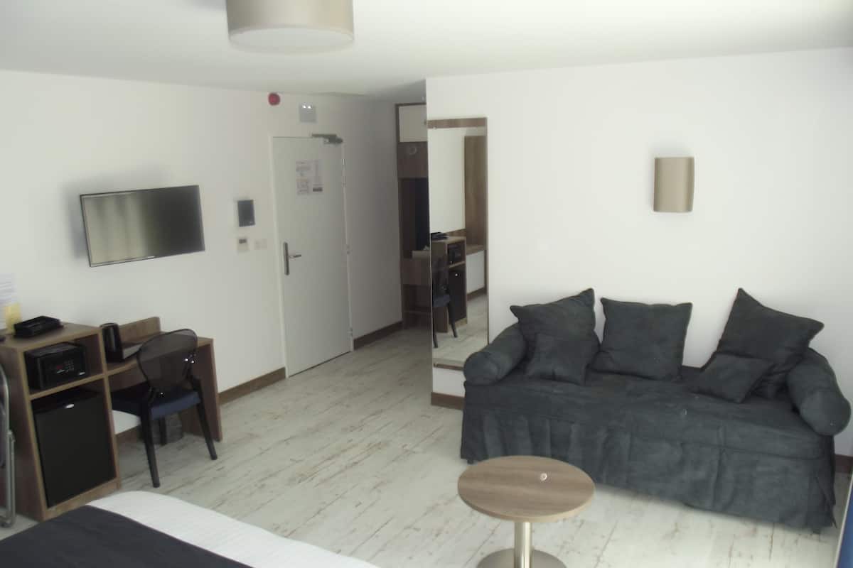 A hotel room with a bed, a desk with a chair, a small round table, a sofa, and a TV mounted on the wall.