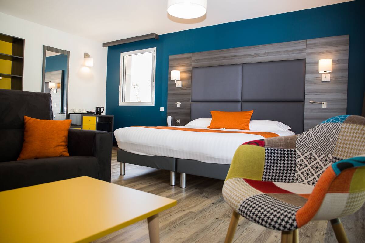 A modern hotel room with a bed, a sofa, a chair, and a small table.