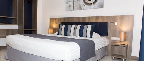 A modern hotel room with a large bed, a wooden headboard, two bedside tables with lamps, and a wall-mounted abstract art piece.
