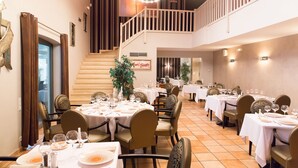 A dining area with multiple tables set for guests, a staircase, and a view of the outdoors. - Hotel Restaurant Le Domaine des Oliviers (Pierrelatte)