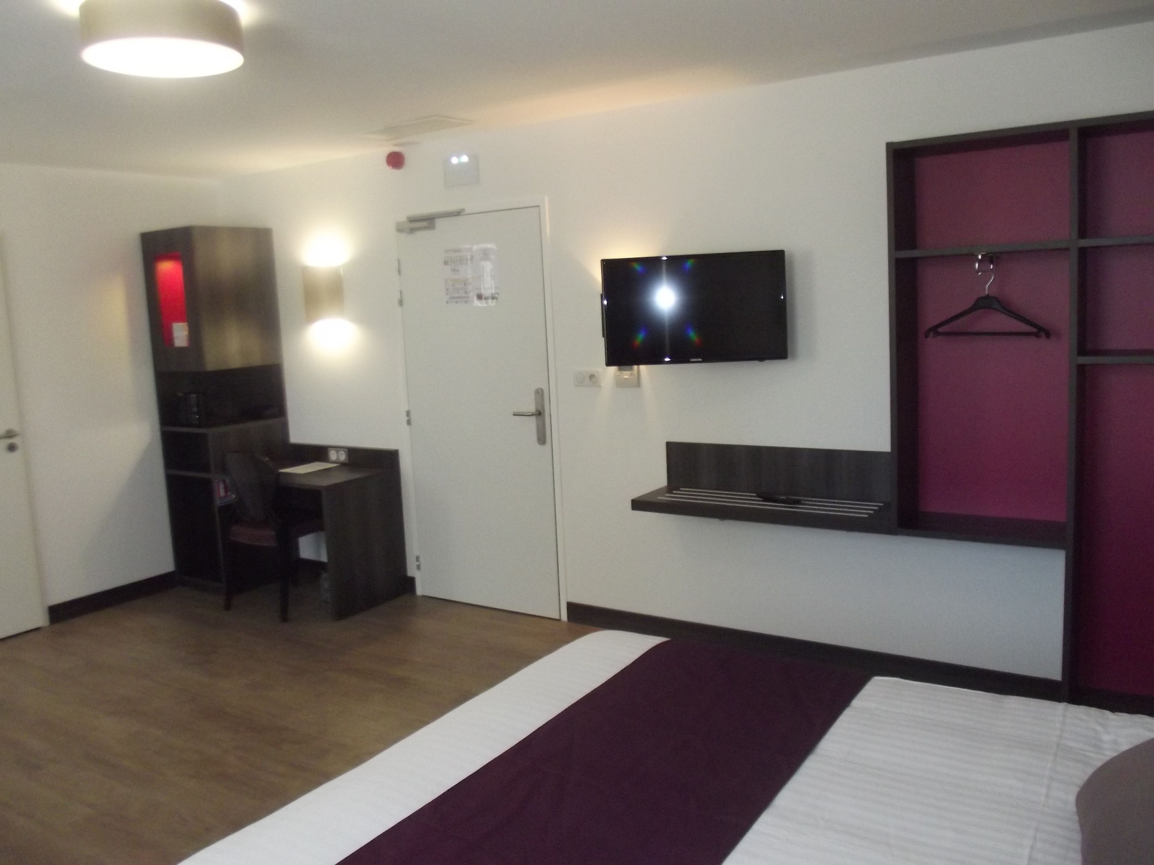 A hotel room with a bed, a desk, a television, and a wardrobe.