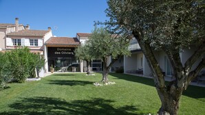 A property with a well-maintained lawn, a large tree, and a building with a sign reading "Domaine des Oliviers". - Hotel Restaurant Le Domaine des Oliviers (Pierrelatte)