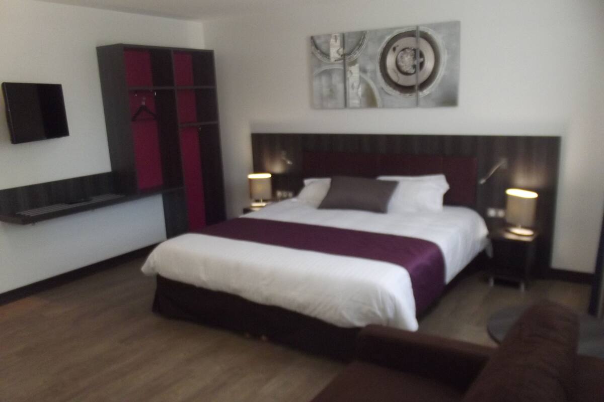 A modern hotel room with a large bed, a wardrobe, a flat-screen TV, and a painting on the wall.