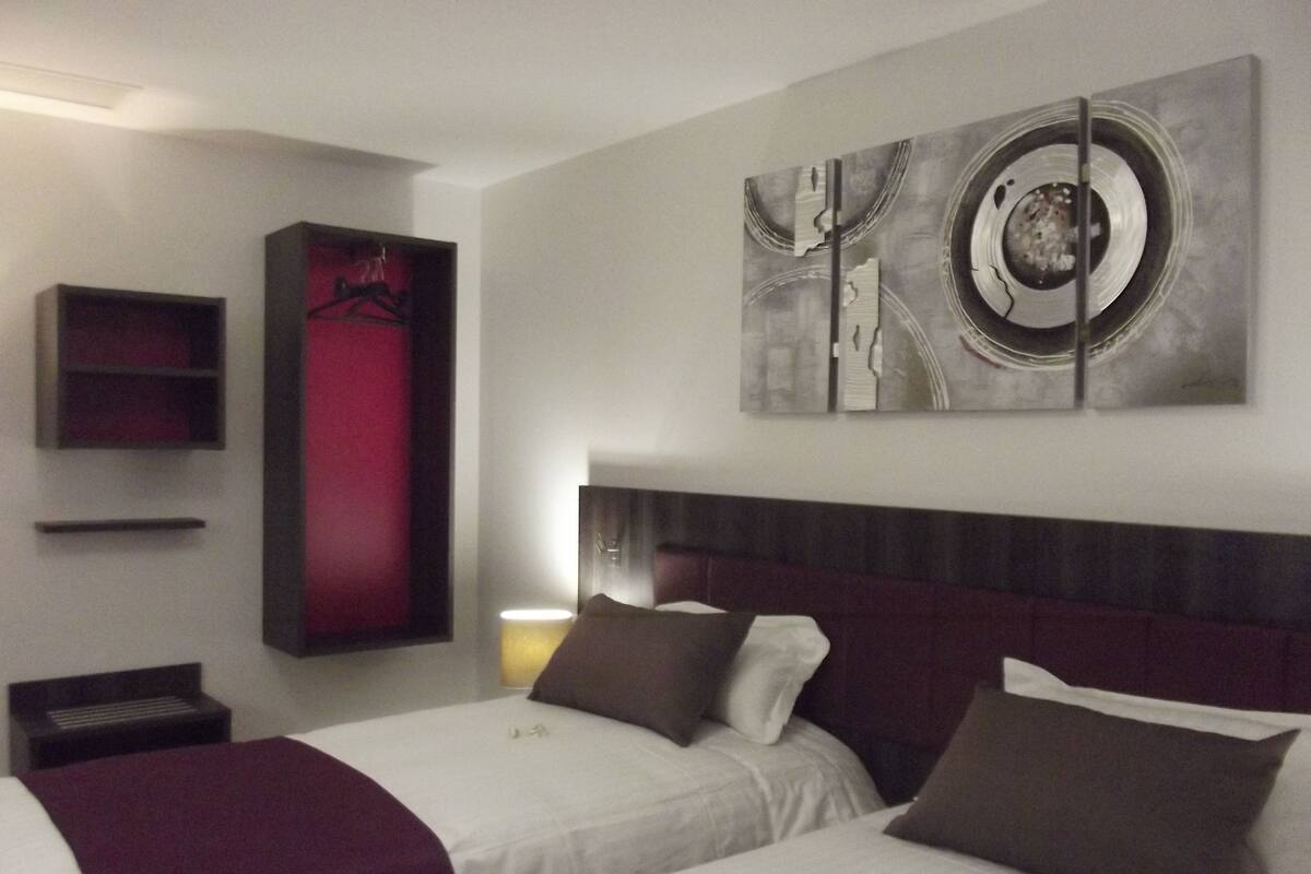 A hotel room with two beds, a red accent wall, and a large abstract painting above the beds.