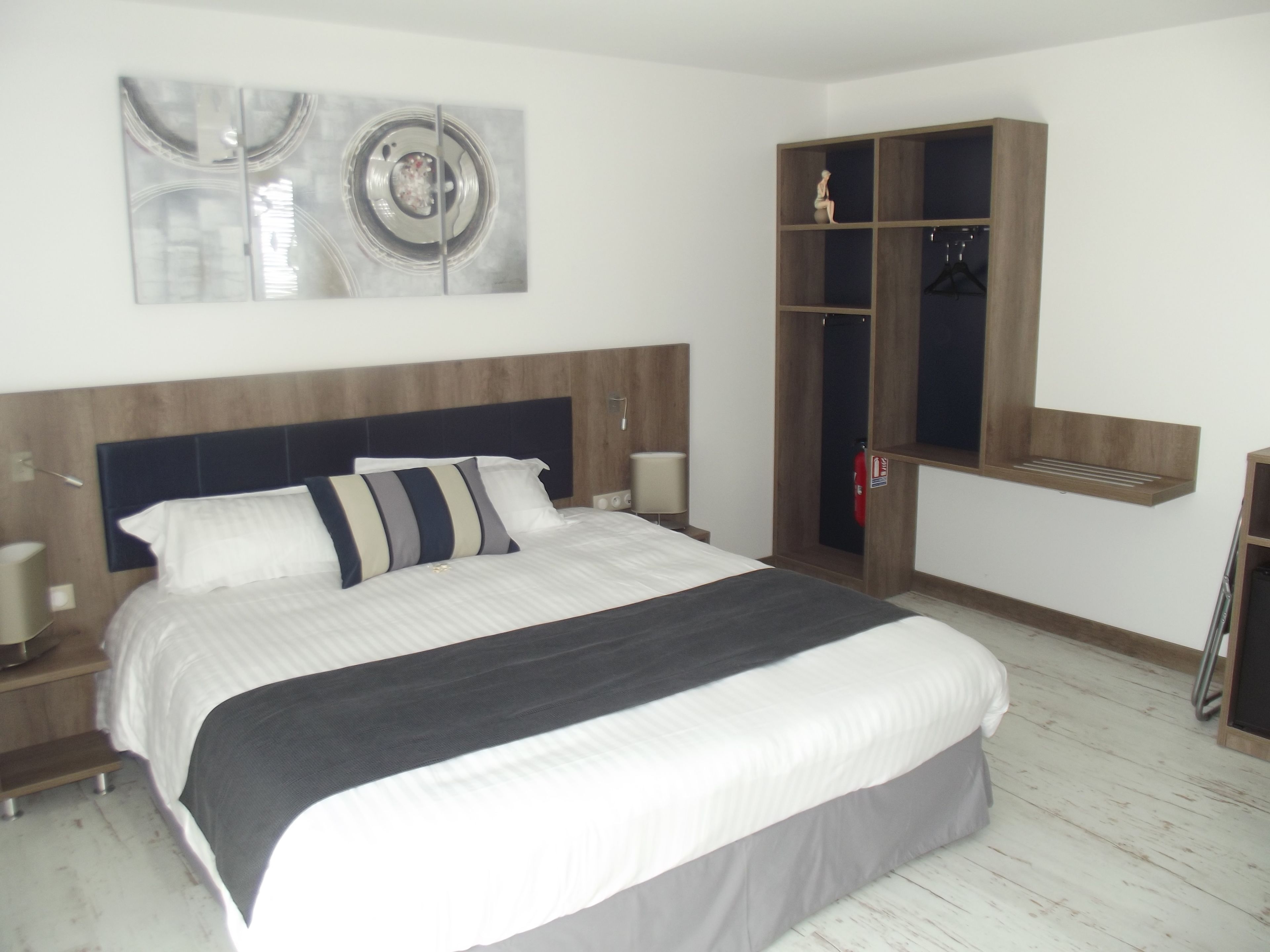 Quarto moderno com cama grande, guarda-roupa de madeira e prateleira na parede.