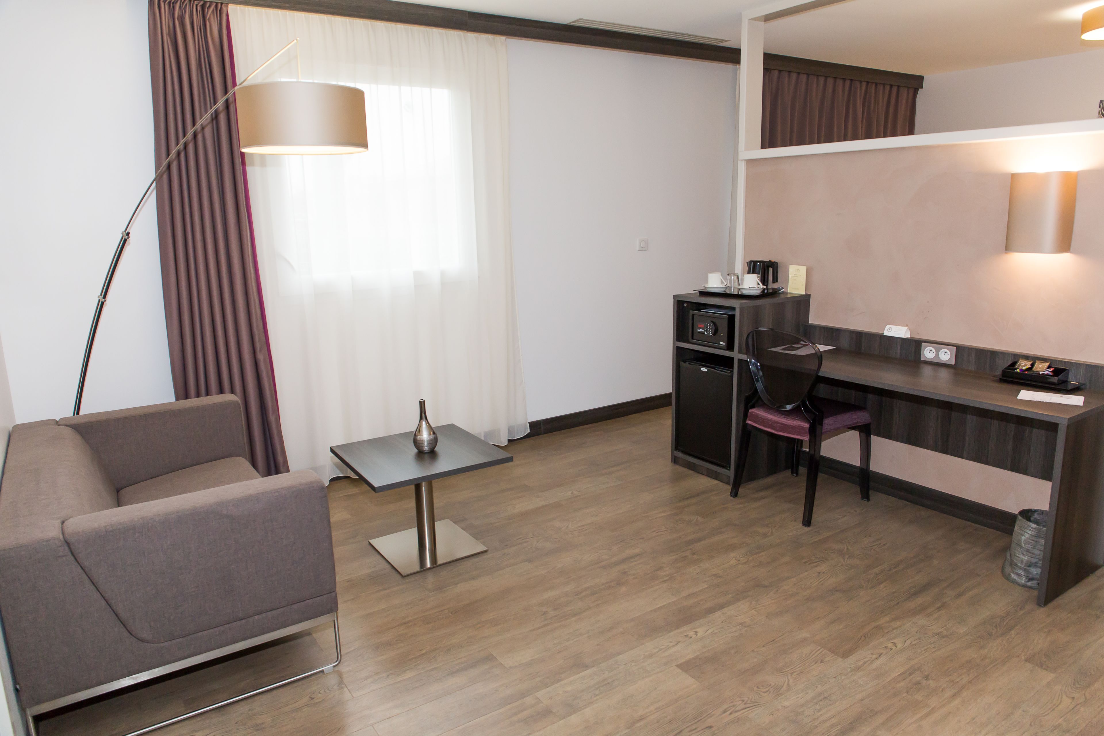 Een kleine hotelkamer met een slaapbank, een tafeltje, een bureau met een stoel, een magnetron en een prullenbak.