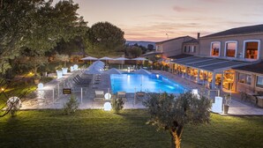 A swimming pool with lounge chairs and umbrellas, surrounded by a landscaped garden and a building with outdoor seating. - Hotel Restaurant Le Domaine des Oliviers (Pierrelatte)