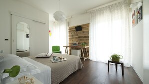A bedroom with a bed, a desk, a chair, a small table with a plant, and a mirror. - Nice Hotel Bibione (San Michele al Tagliamento)