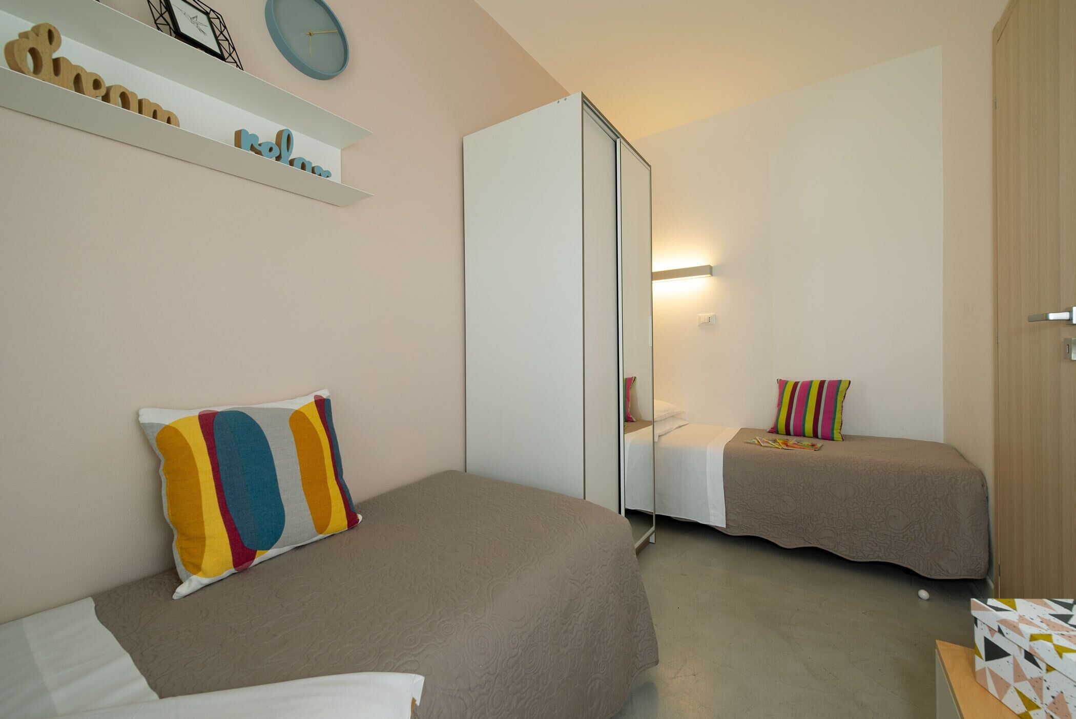 Un dormitorio con dos camas, un armario, un espejo y una estantería con objetos decorativos.