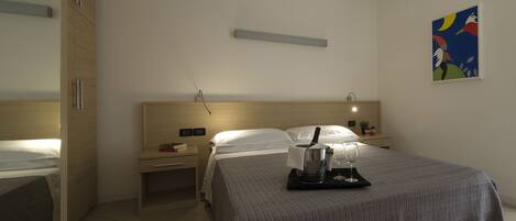 A hotel room with a bed, bedside tables, a nightstand, a lamp, a painting, and a tray with glasses and a pitcher.