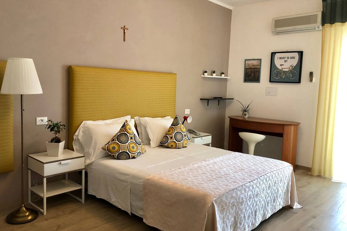 A neatly arranged bedroom with a bed, bedside tables, a lamp, a desk, and a chair.