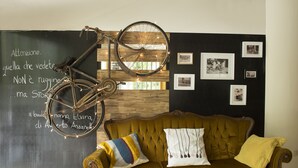 A room with a vintage bicycle hanging on a chalkboard, a tufted sofa with colorful cushions, and a wall adorned with framed photographs. - Nice Hotel Bibione (San Michele al Tagliamento)