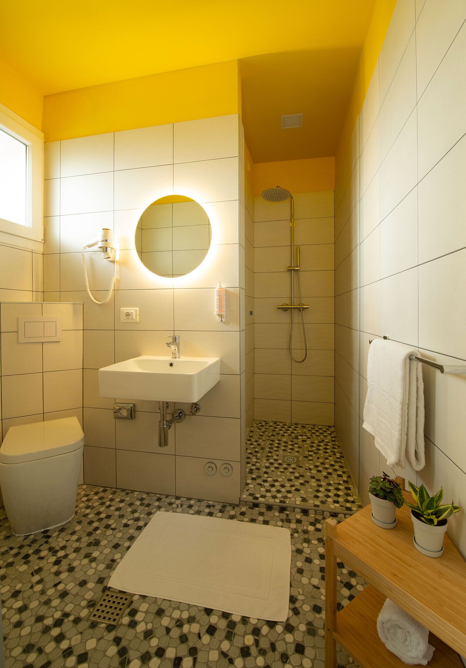Un baño con lavamanos blanco, un espejo, una ducha y suelo de baldosas.