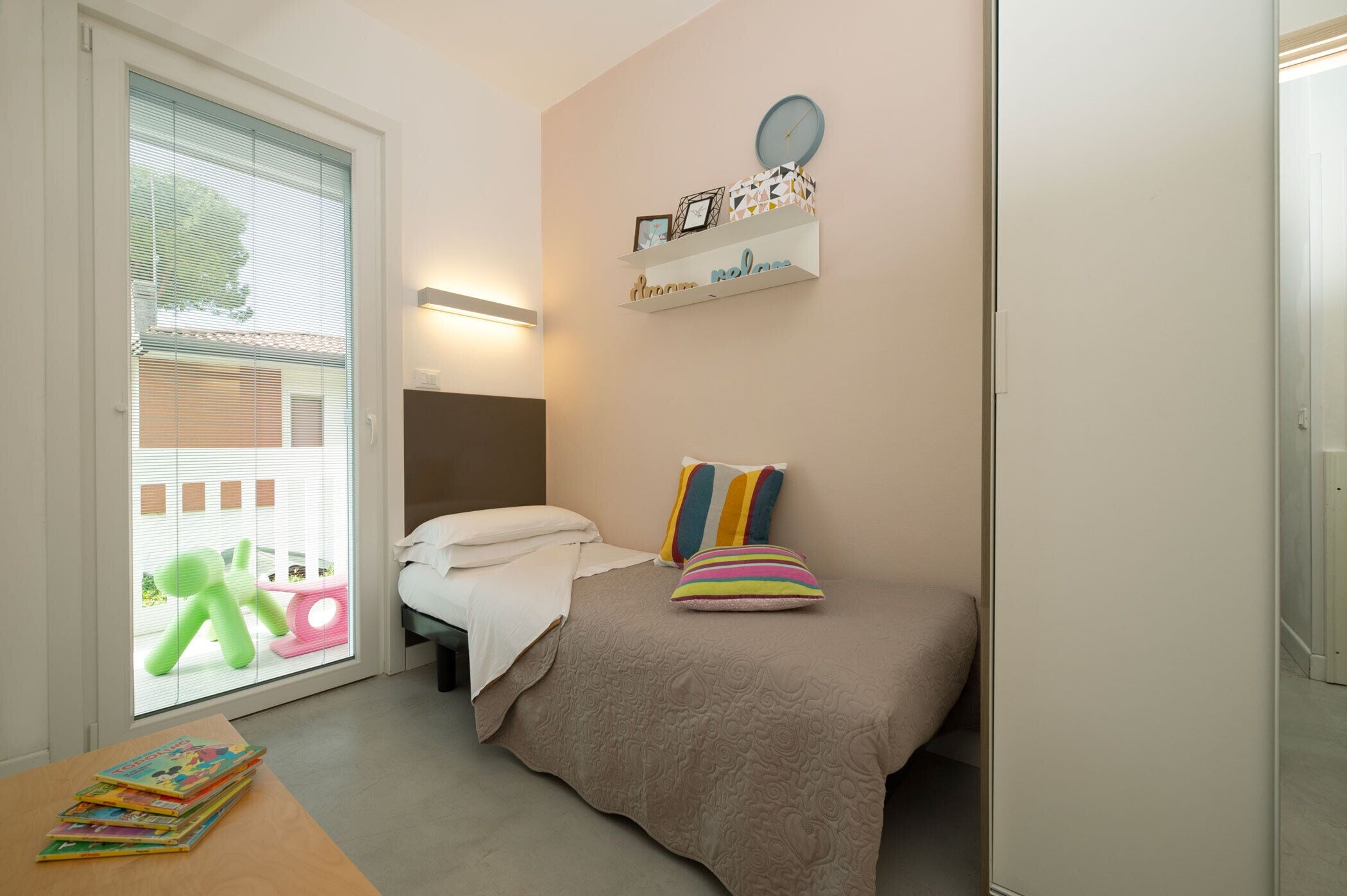 Een slaapkamer met een bed, nachtkastje en een raam met jaloezieën.