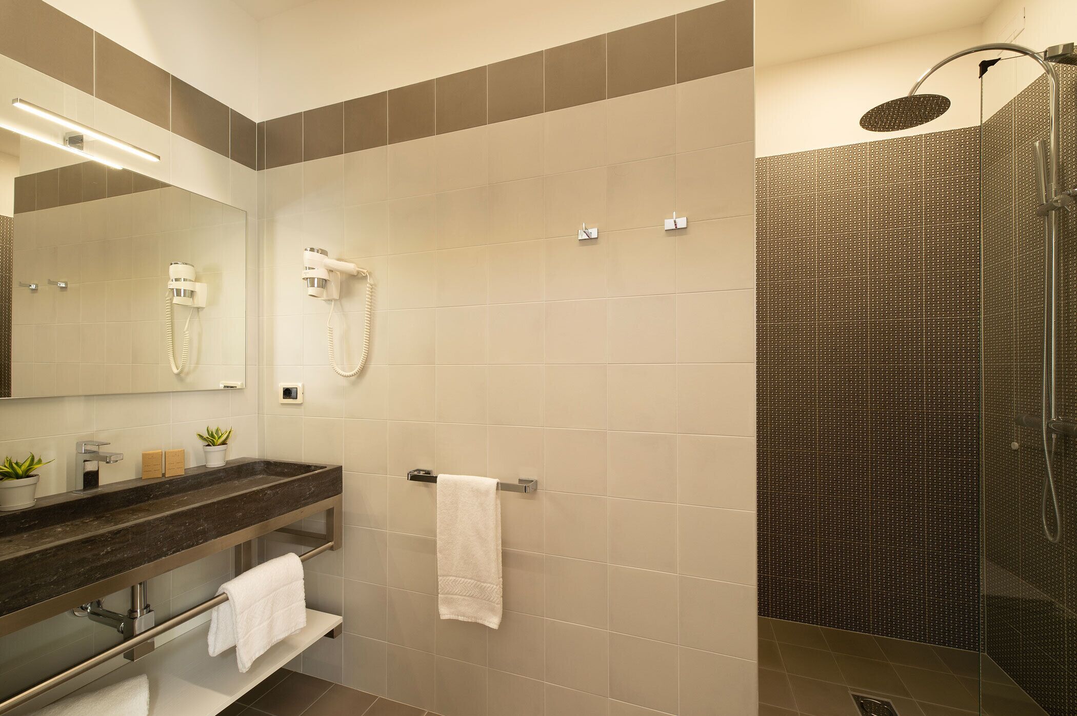 A modern bathroom with a glass shower enclosure, a vanity with a dark countertop, and a mirror above the sink.