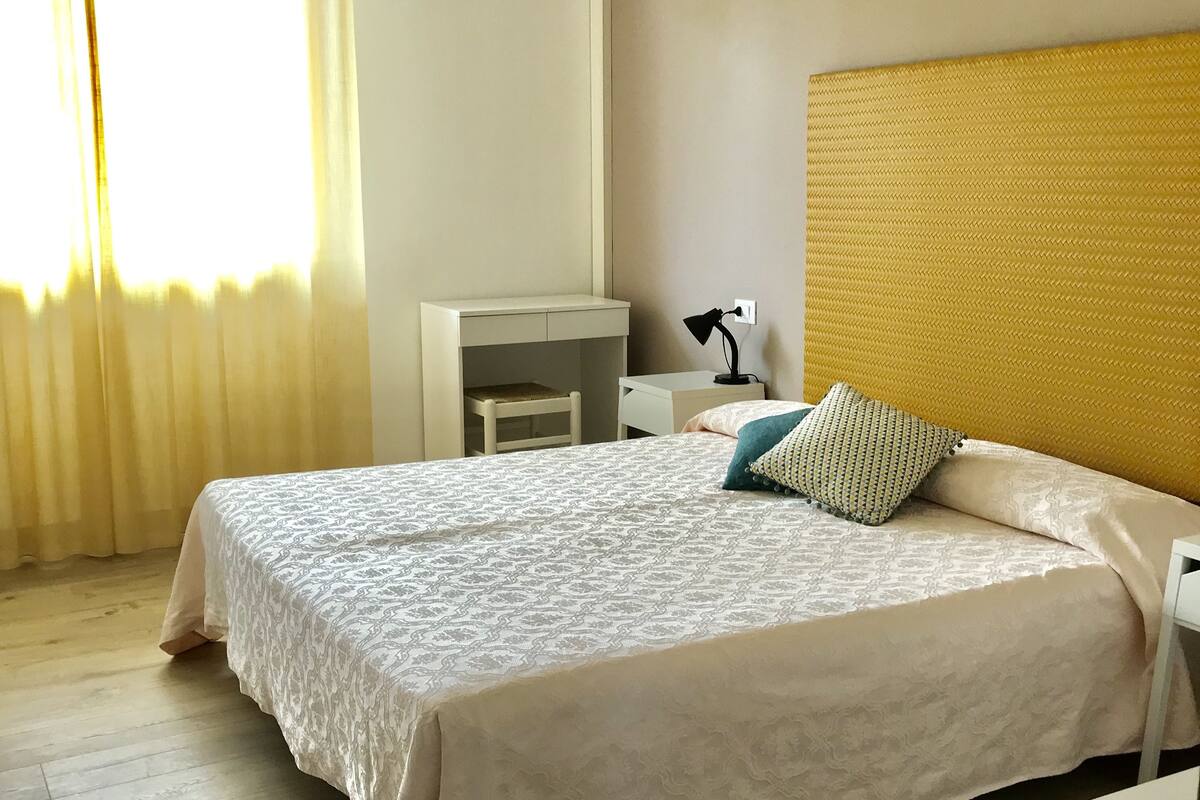 A neatly arranged bedroom with a large bed, a bedside table with a lamp, and a small desk.