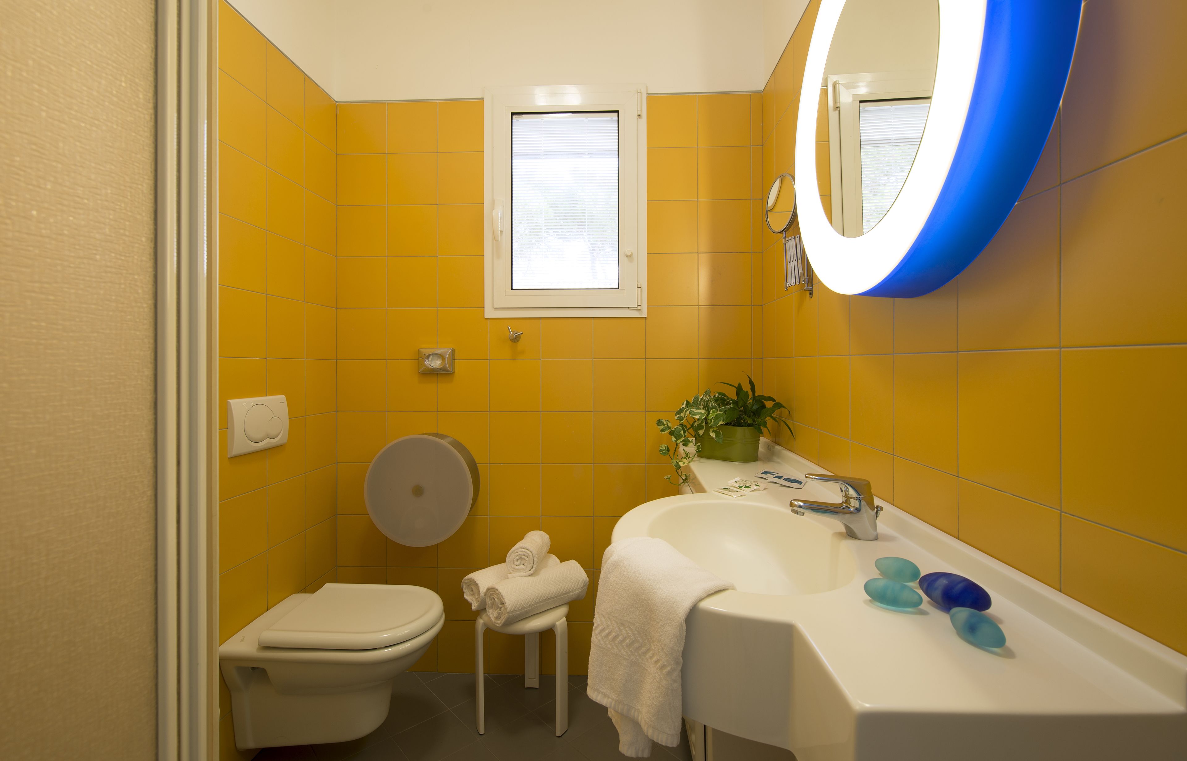 A bathroom with yellow walls, a white toilet, a sink with a mirror, and a window above the toilet.