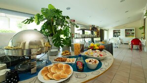 A buffet setup with various food items, a large plant, and a kitchen area in the background. - Nice Hotel Bibione (San Michele al Tagliamento)