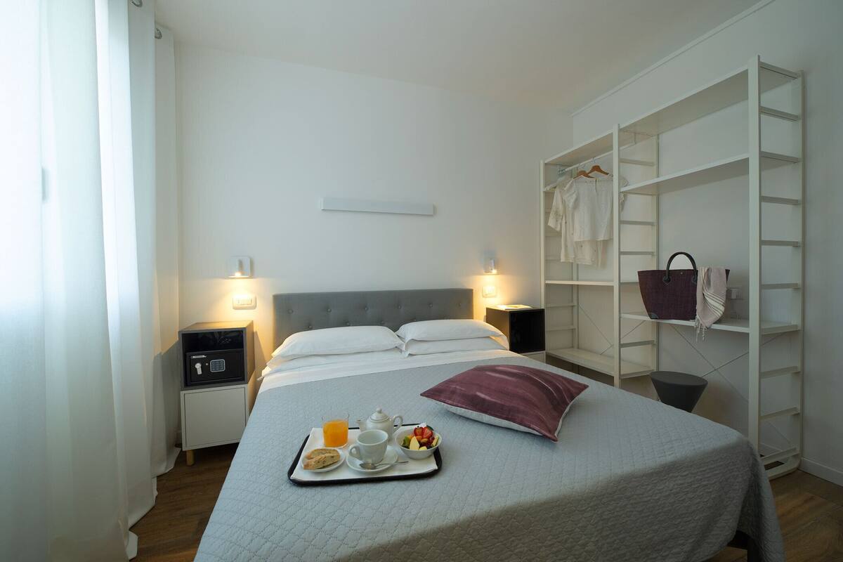 A hotel room with a bed, bedside tables with lamps, a wardrobe, and a tray with breakfast items.