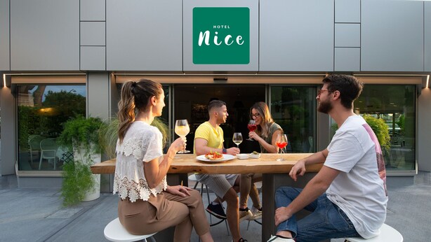 A group of people dining at an outdoor table in front of a building with a sign that reads "HOTEL Nice". - Nice Hotel Bibione (San Michele al Tagliamento)