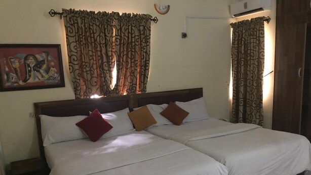 A double bed with white linens and three pillows, a wooden headboard, and patterned curtains. - City Travels Inn (Abuja)
