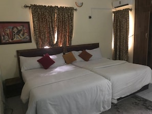 A double bed with white linens and three pillows, a wooden headboard, and patterned curtains. - City Travels Inn (Abuja)