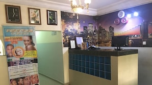 A hotel reception area with a cityscape mural, a reception desk, and a poster advertising a beauty salon. - City Travels Inn (Abuja)