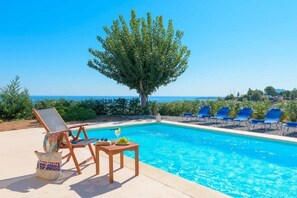 A poolside area with a clear view of the sea, a large tree, and several lounge chairs. - Villa Zizi Sea View (Rhodes)