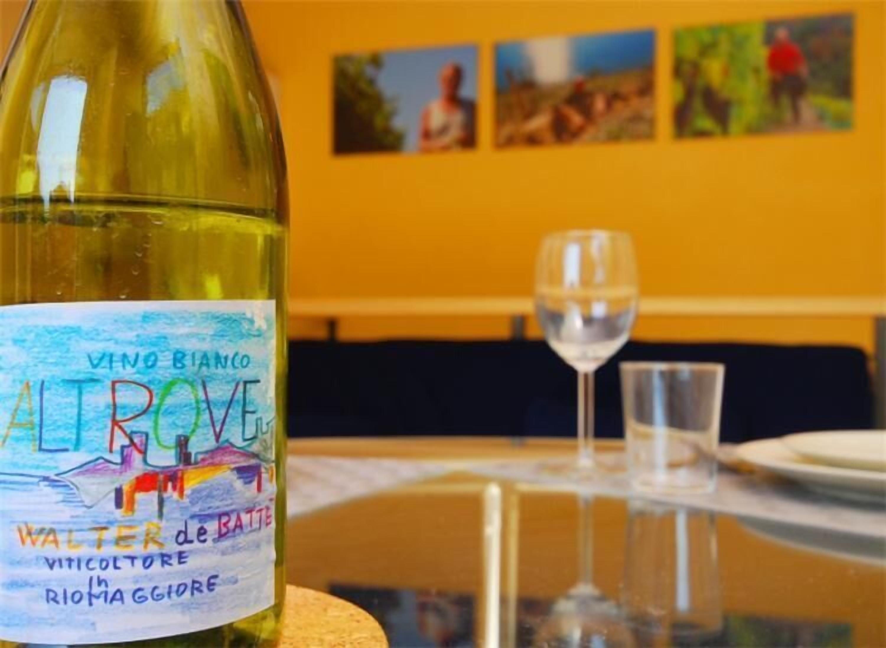 Una botella de vino con etiqueta colorida, una copa y una mesa con una pared amarilla al fondo.