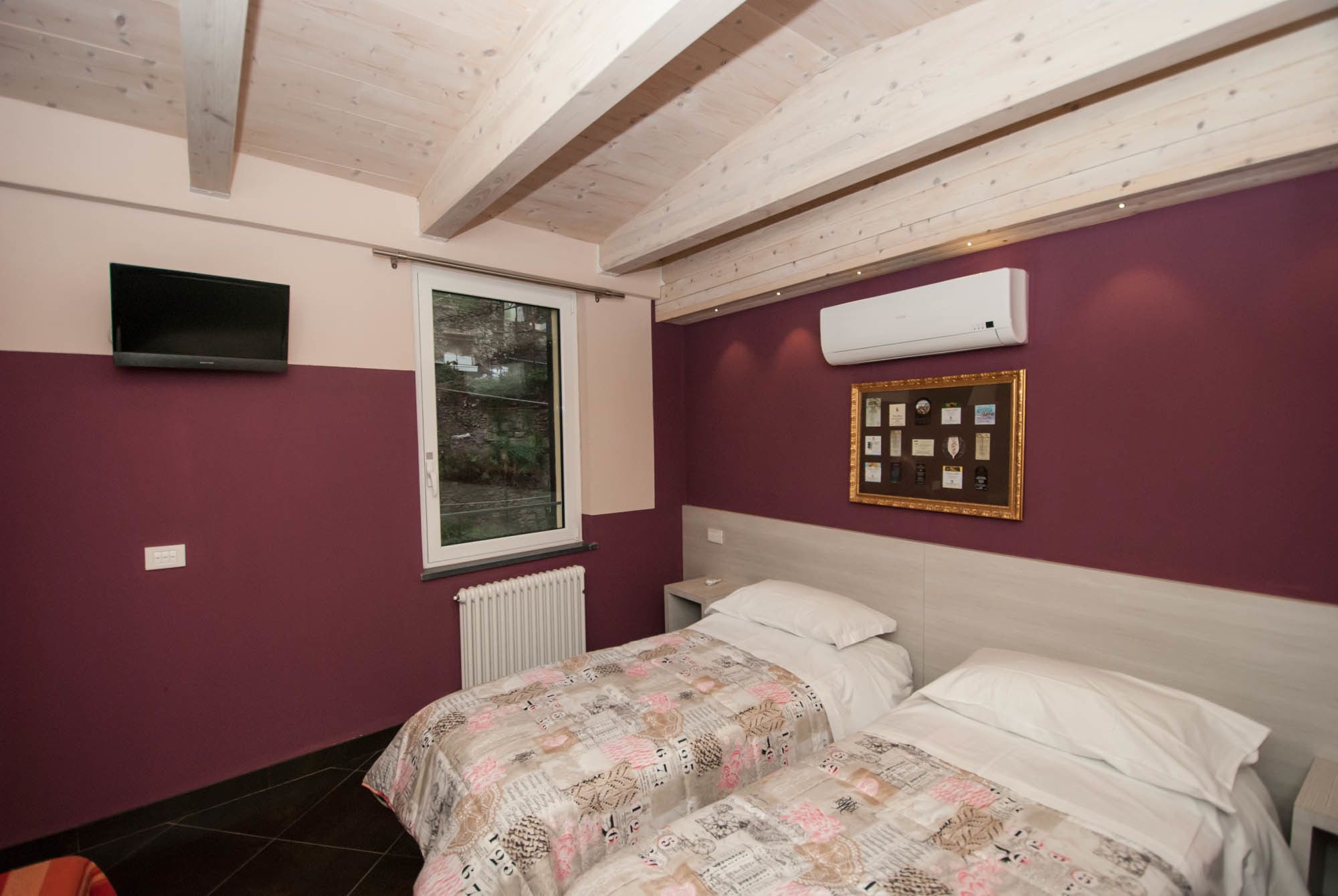 A bedroom with a bed, a window, an air conditioner, and a framed certificate on the wall.