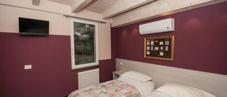 A bedroom with a bed, a window, an air conditioner, and a framed certificate on the wall.