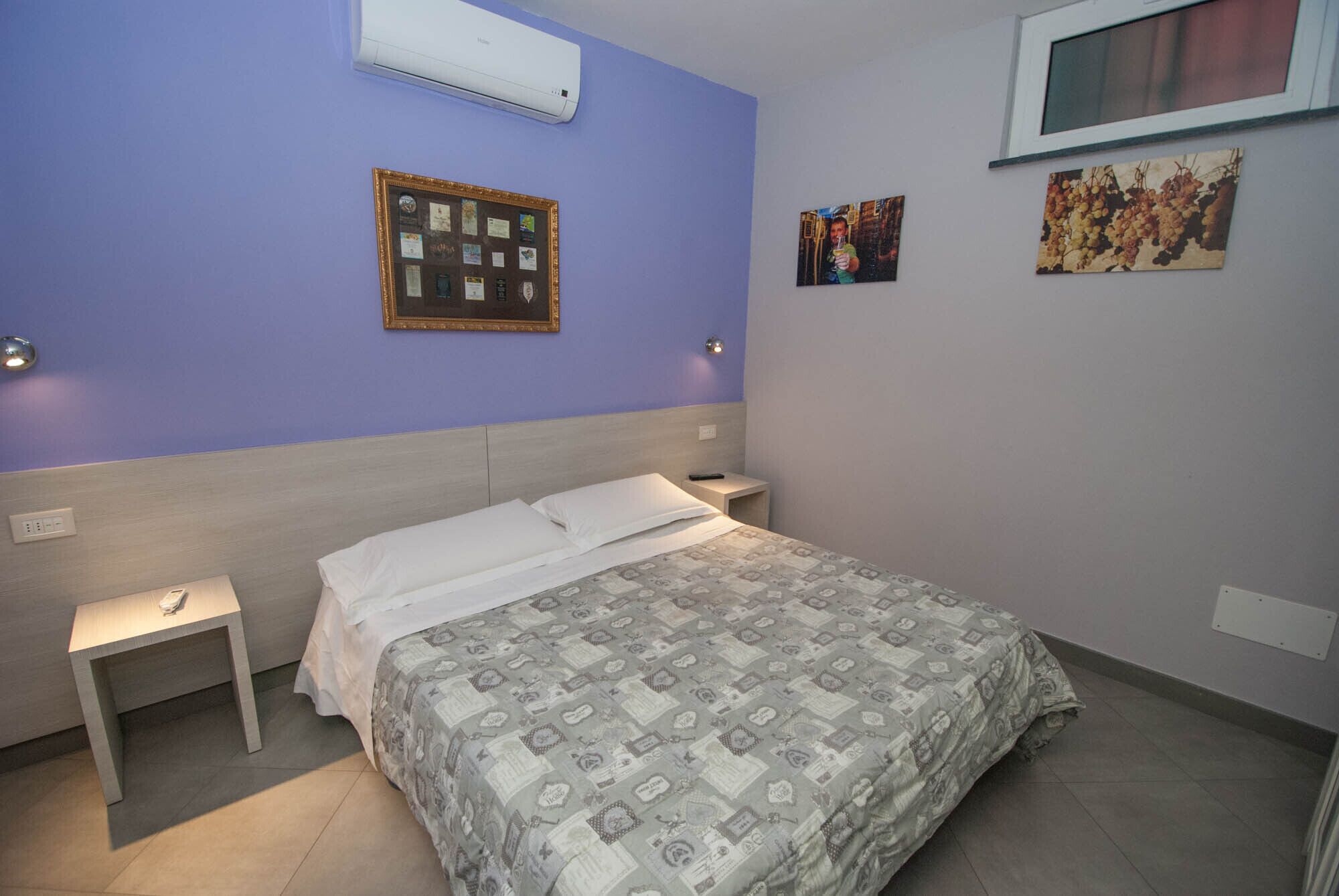 A bedroom with a bed, a nightstand, a wall-mounted air conditioner, and framed pictures on the wall.