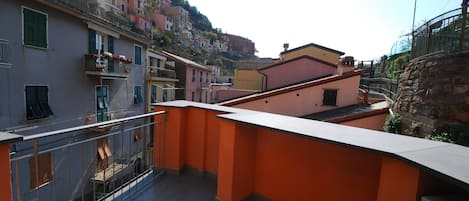A rooftop terrace with a stone wall, a metal railing, and a view of colorful buildings in the background.