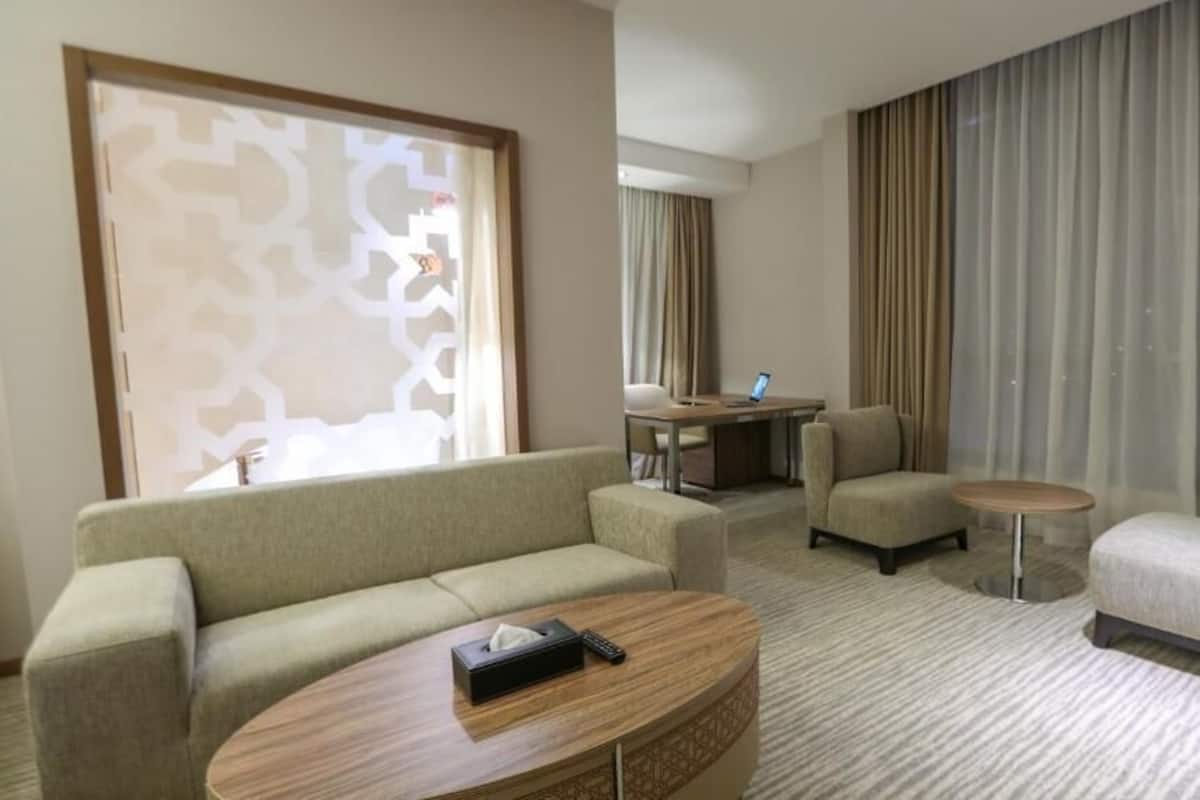 A hotel room with a sofa, armchairs, a small table, and a desk with a laptop.