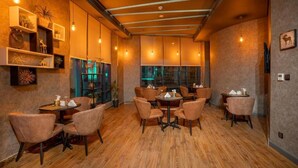 Een restaurant met houten vloer, verschillende tafels en stoelen, hangende lampen en planken met decoratieve objecten.