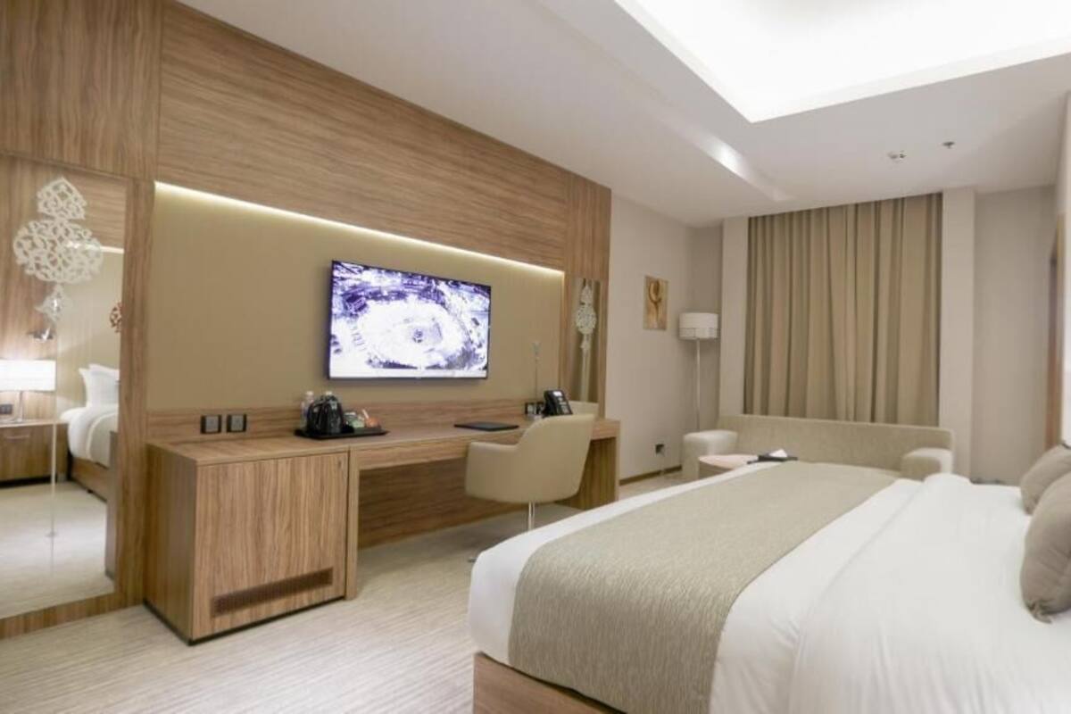A modern hotel room with a large bed, a desk, a television, and a seating area.