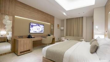 A modern hotel room with a large bed, a desk, a television, and a seating area.
