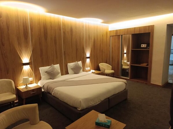 Ein Hotelzimmer mit einem großen Bett, Nachttischlampen, einer Wandpaneele aus Holz, einer Sitzecke mit Sesseln und einem Kleiderschrank.