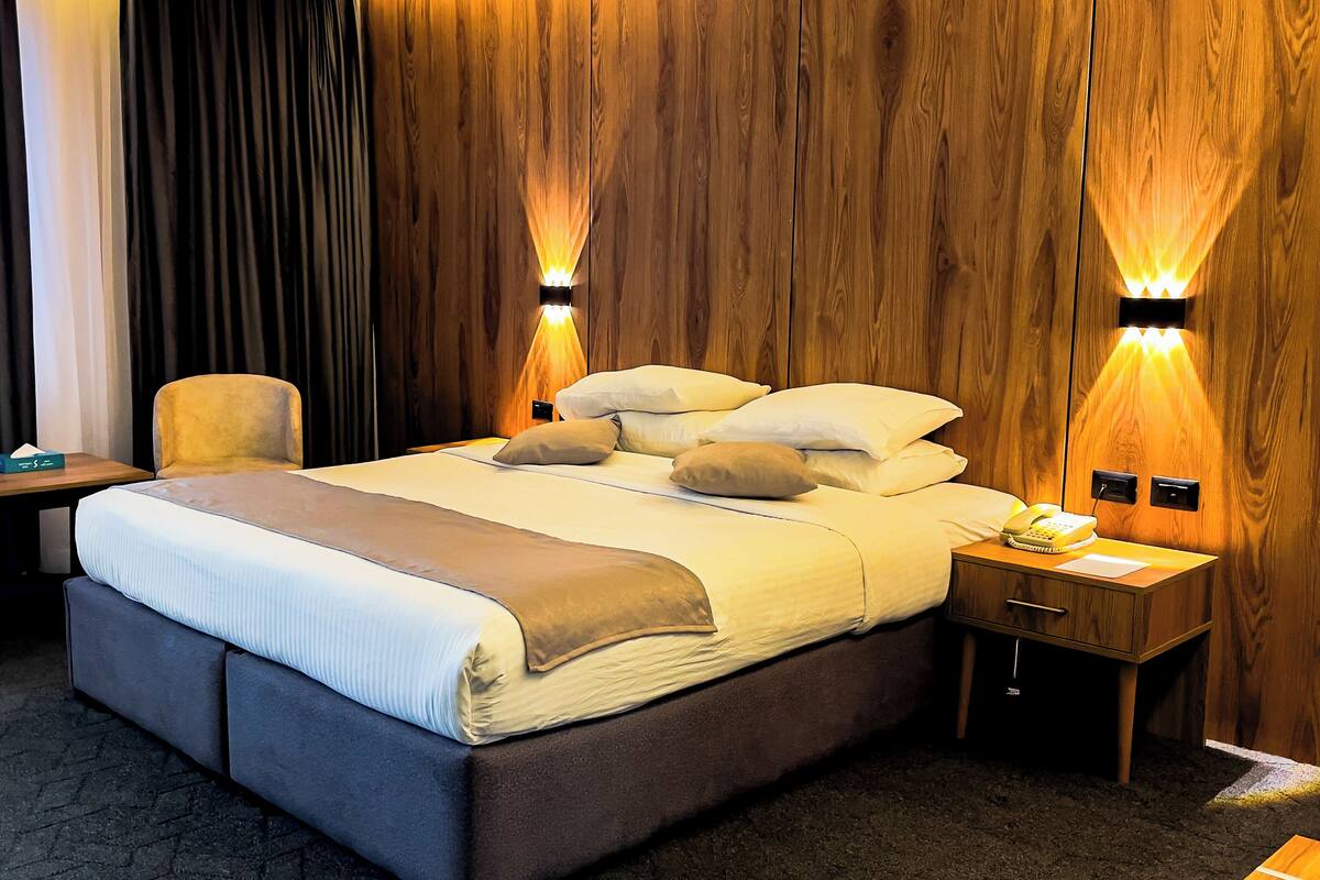 Een hotelkamer met een groot bed, twee nachtkastjes, een stoel en houten lambrisering.