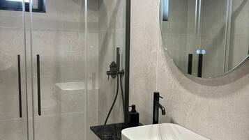 Un baño moderno con ducha de vidrio, lavamanos blanco y espejo redondo.