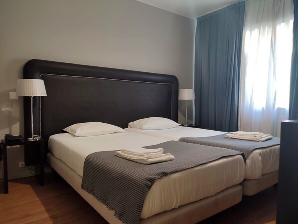 Habitación de hotel con una cama grande, dos mesitas de noche, una lámpara y una ventana con cortinas.