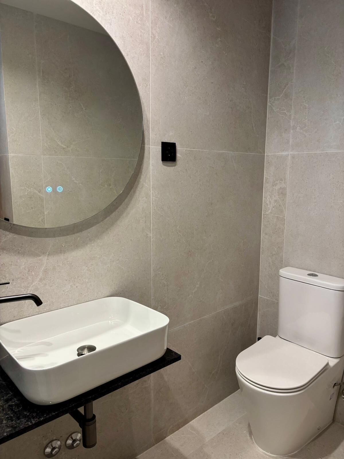 Un baño con un lavamanos blanco, un inodoro y un espejo redondo.