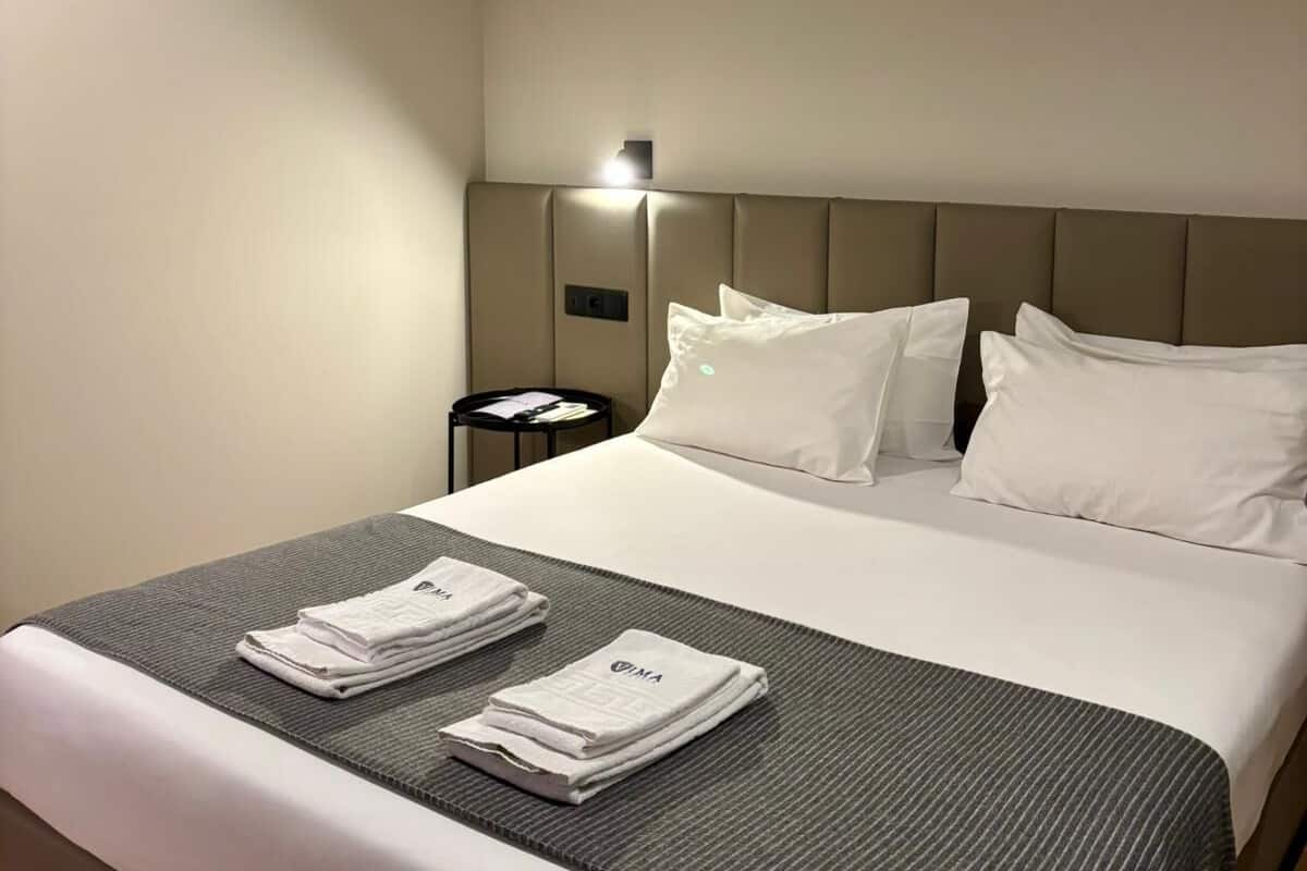 A hotel room with a neatly made bed, a bedside table with a lamp, and a small round table with a chair.