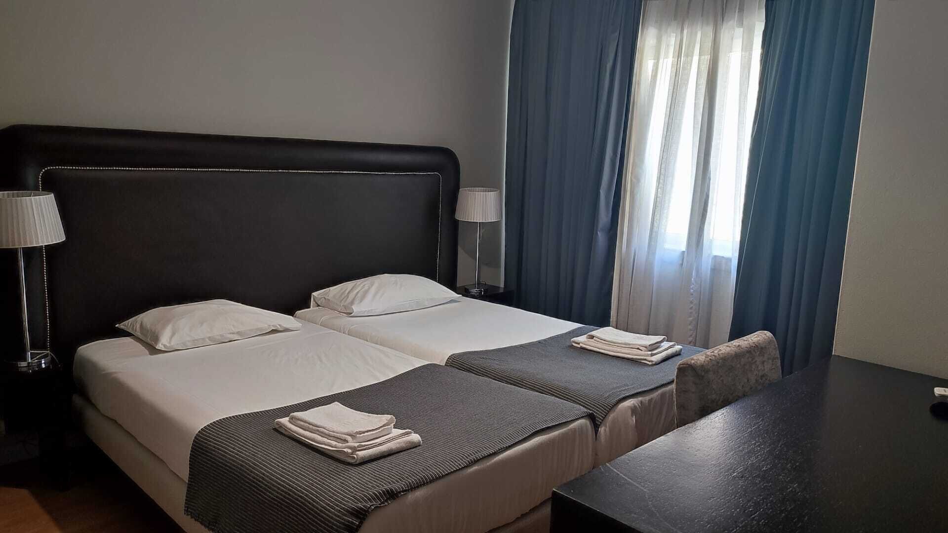 A hotel room with two beds, a desk, and a lamp.