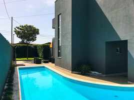 Un edificio moderno con piscina, mobiliario exterior y un árbol.