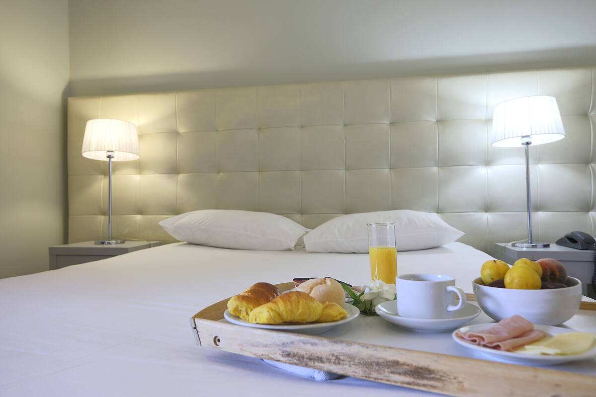 A neatly made bed with a headboard, a tray with croissants, a glass of orange juice, a cup, and a bowl of fruit.