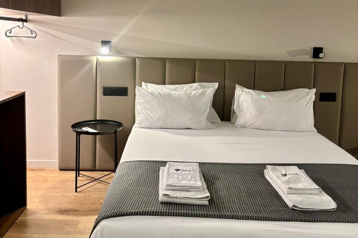 A hotel room with a bed, a small table, a hanging light, and a wall-mounted control panel.