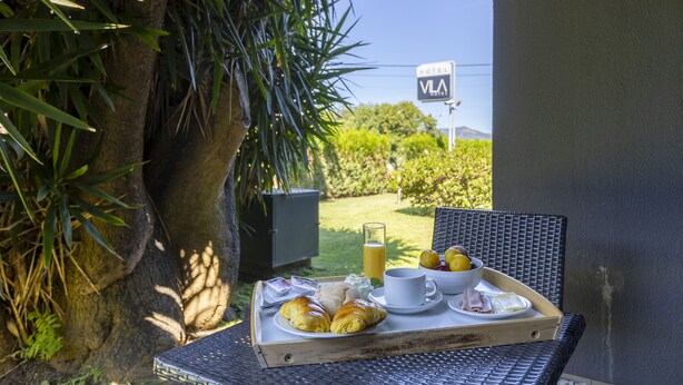 En frukostbricka står på ett bord med croissanter, en kopp, ett glas apelsinjuice och en skål med frukt. I bakgrunden syns en skylt med texten ”VIA Hotel”.
